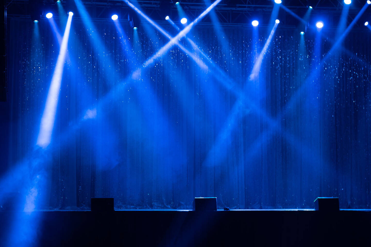 Blue stage lights illuminate a dark curtain with sparkling particles in the air.